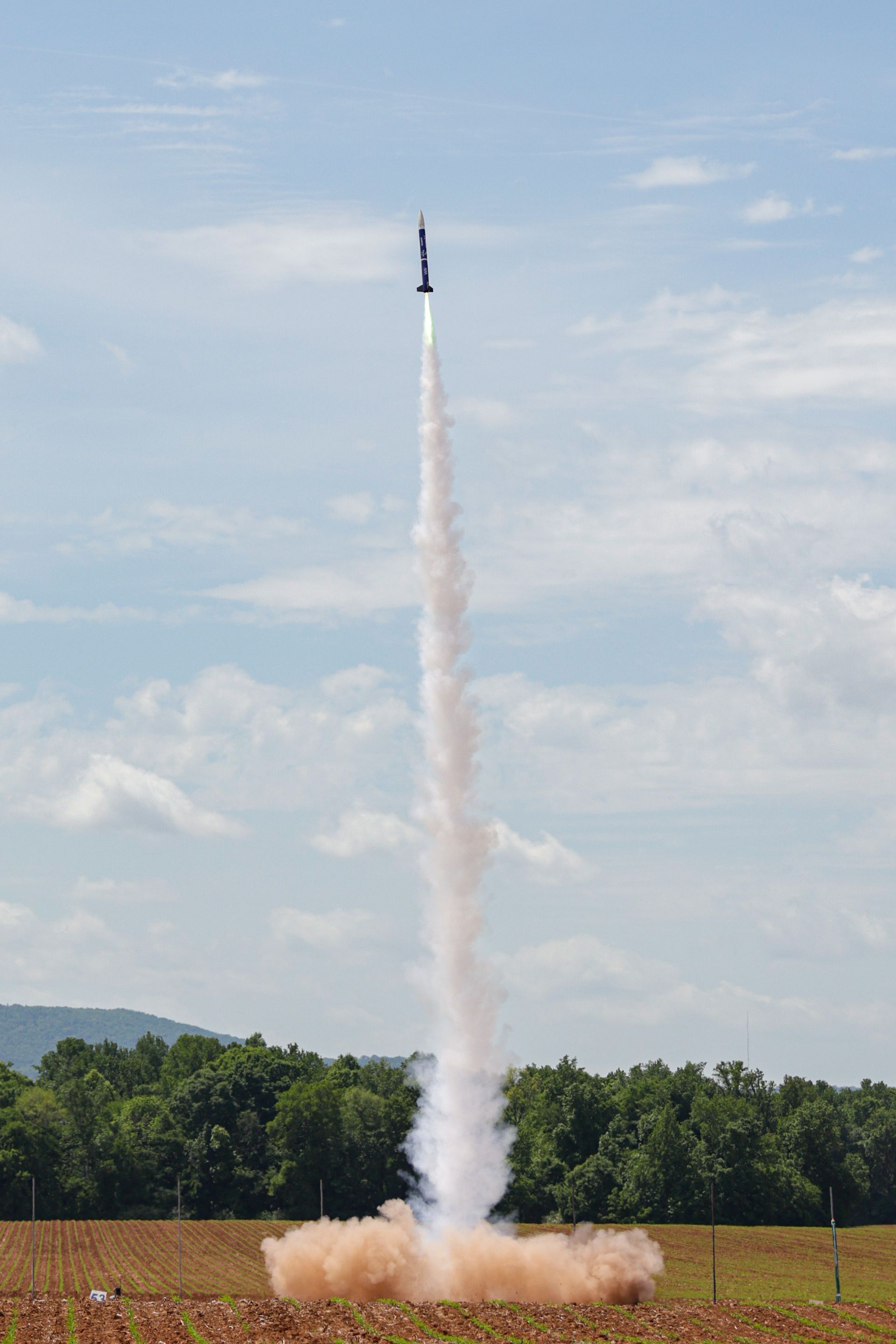 An AURA rocket lifting off from the pad, trailing a column of smoke